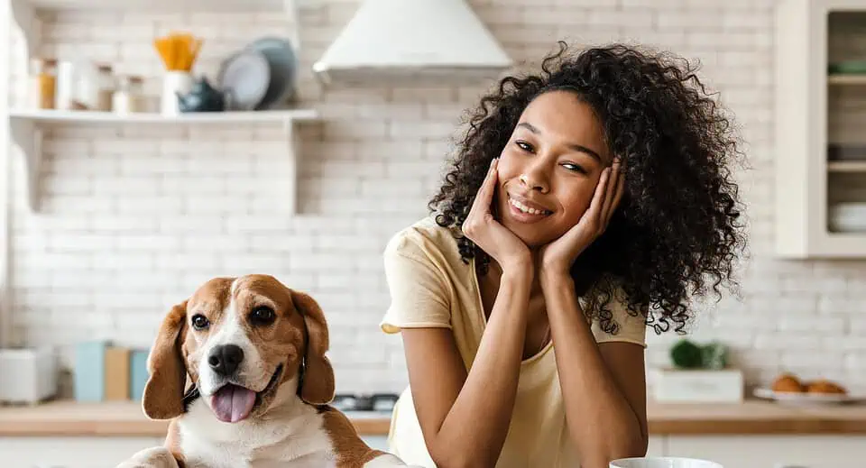 Smiling young woman leaning on a kitchen counter with her pet beagle - best kidney diet for dogs