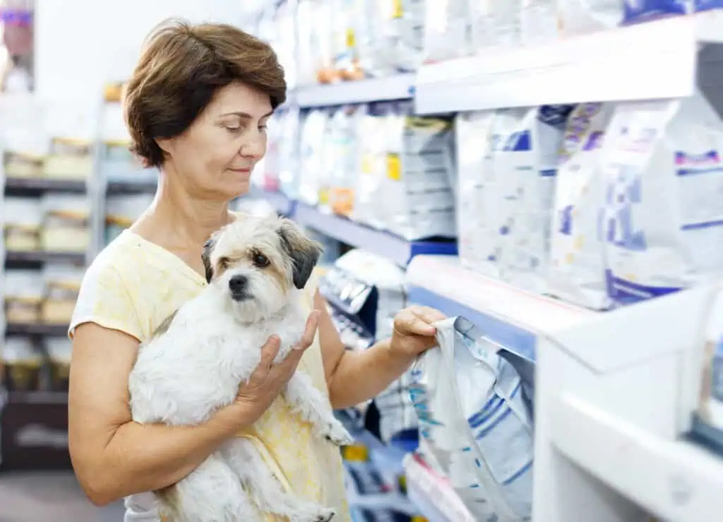 Elderly woman choosing dog food for her puppy in pet supplies store - pet stockpile